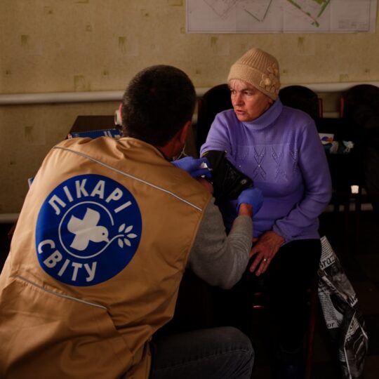 Ein Mitarbeitender misst den Blutdruck bei einer älteren Dame.