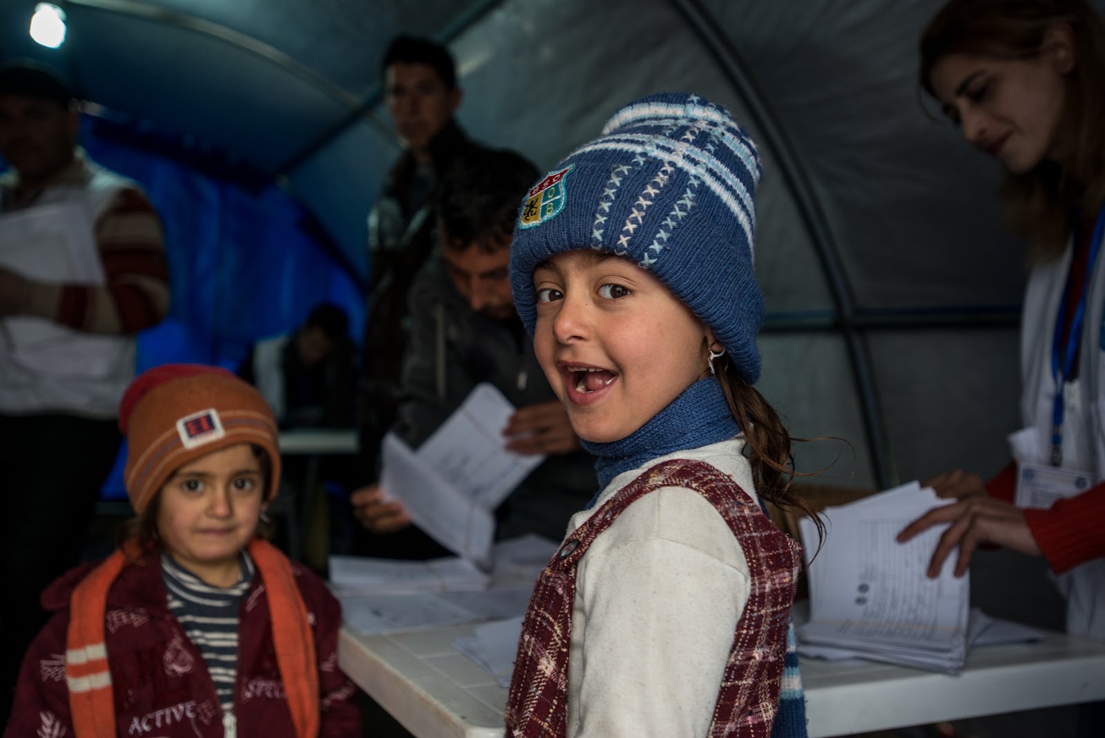 Irak: Im Vordergrund Kinder in warmen Klamotten, im Hintergrund Erwachsene beim Verteilen und Organisieren von Hilfsgütern in einem Zelt. Im Irak leistet Ärzte der Welt medizinische Hilfe. © Guillaume Pinon