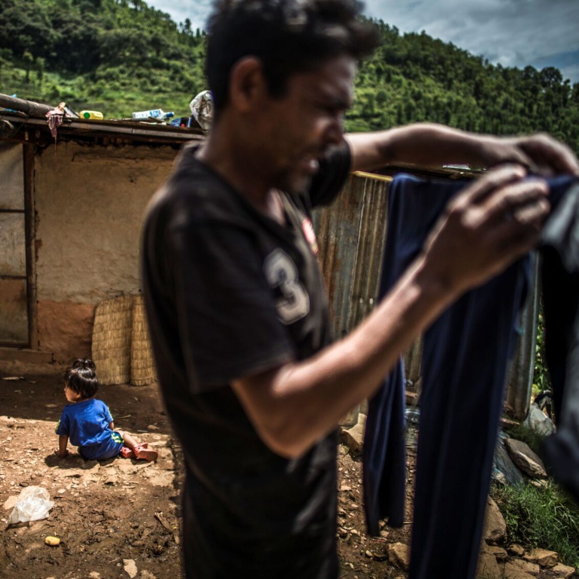 Nepal: Ein Mann hängt Wäsche auf, im Hintergrund sitzt ein Kind auf dem Boden. © Olivier Papegnies