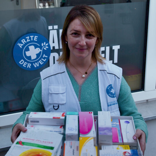 open.med München: Eine Ehrenamtliche von Ärzte der Welt hält eine Box voller Medikamente hoch. © Till Mayer