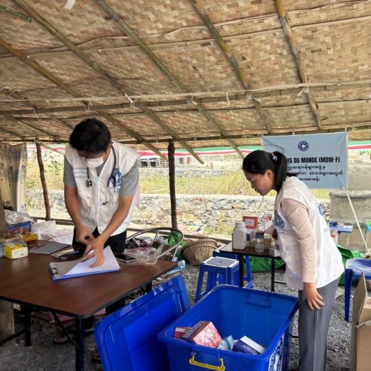 Myanmar: Mitarbeiter*innen stehen in einer mobilen Klinik von Ärzte der Welt. Neben ihnen stehen Kisten mit Medikamenten und medizinischem Material. © Ärzte der Welt