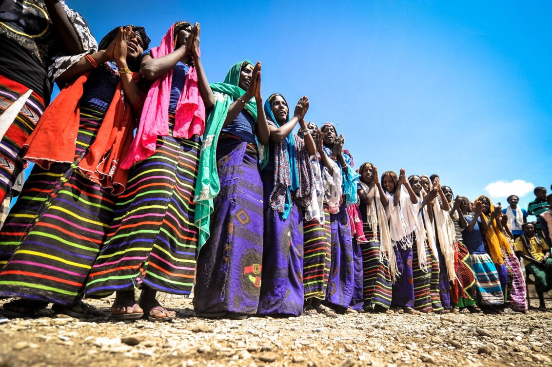 Äthiopien: Eine Gruppe von Menschen in farbenfroher Kleidung mit erhobenen oder gefalteten Händen vor blauem Himmel. In Äthiopien leistet Ärzte der Welt medizinische Hilfe. © Quentin Top