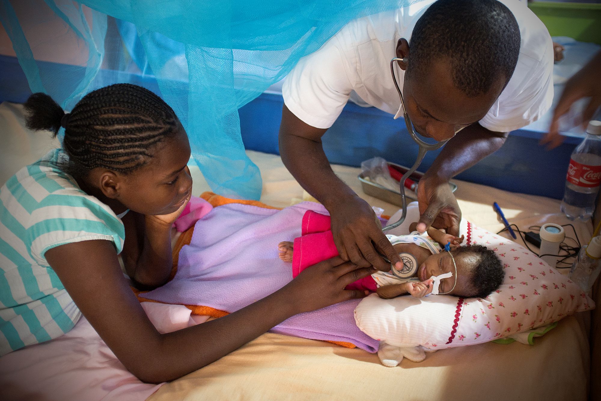 Haiti: Ein Mitarbeiter von Ärzte der Welt hört ein sehr kleines Baby mit dem Stethoskop ab, ein Mädchen sieht zu. © Pierre-W. Henry