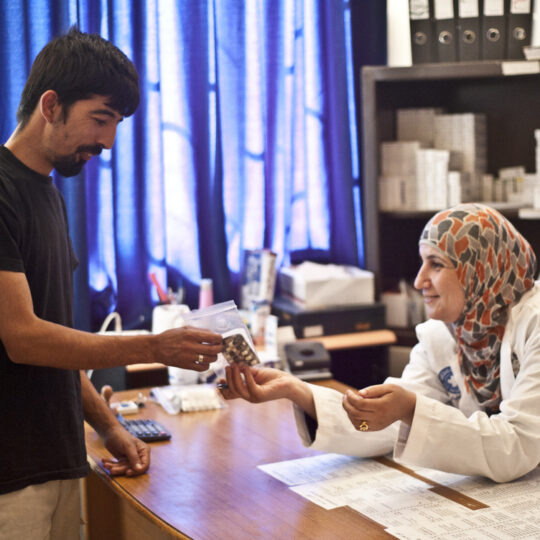 Eine Gesundheitseinrichtung an der syrisch-jordanischen Grenze. Eine Mitarbeiterin von Ärzte der Welt gibt einem Patienten Medikamente. © Sasha Petryszyn