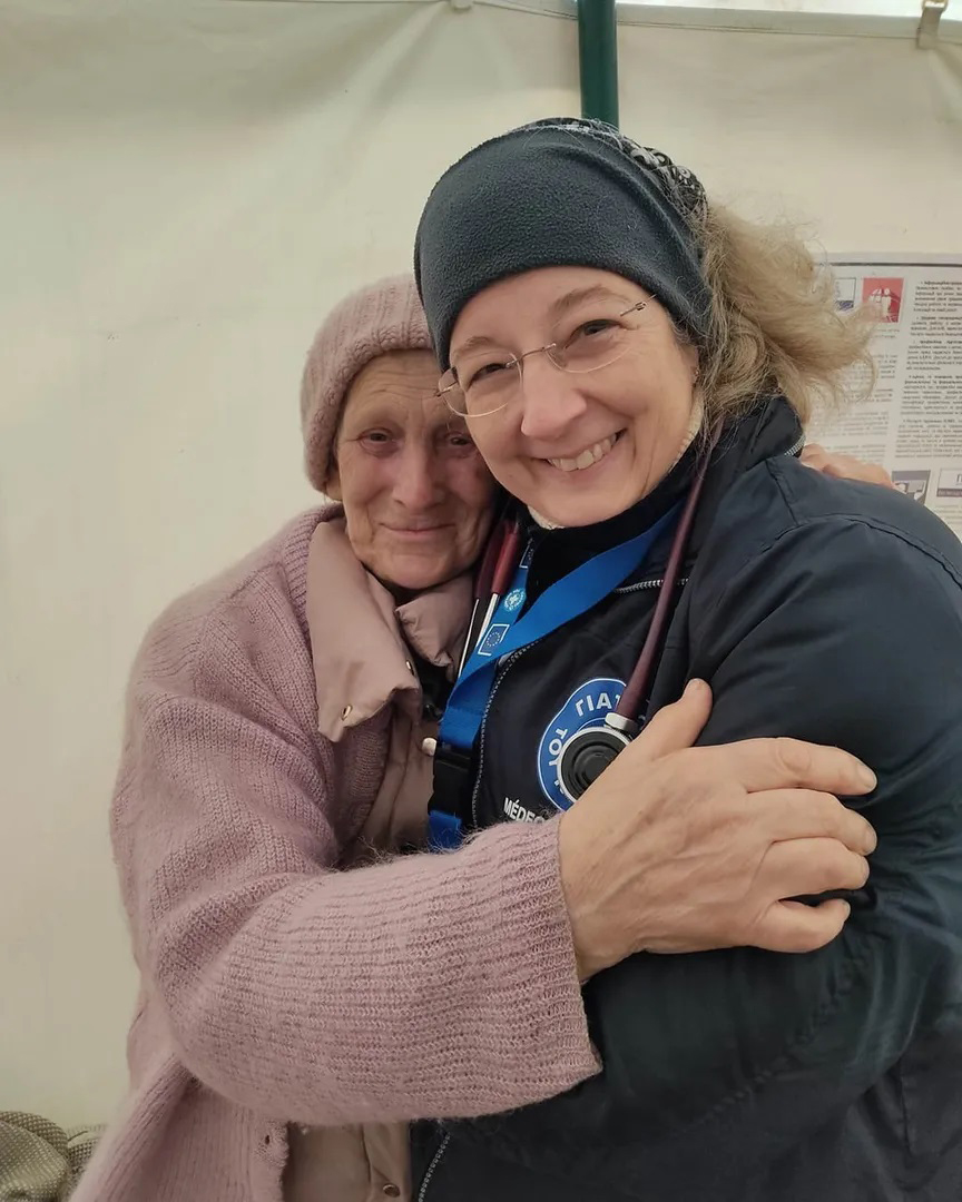 Eine ukrainische Frau umarmt eine Mitarbeiterin von Ärzte der Welt, während beide in die Kamera lächeln. © Yiannis Yiannakopoulos