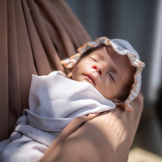 Pakistan: Ein Baby im Arm einer Frau, schlafend. Ärzte der Welt leistet hier medizinische Hilfe. © Saiyna Bashir