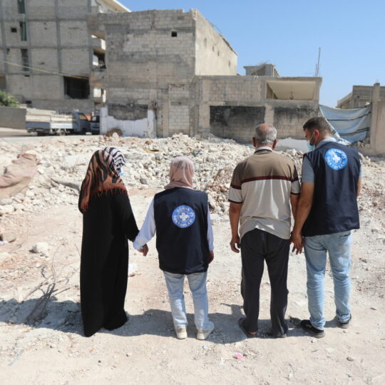 Ein Mitarbeiter und eine Mitarbeiterin von Ärzte der Welt stehen einer Frau und einem Mann bei, während sie vor einem zerstörten Gebäude in Syrien stehen. © Bakr al Kasem