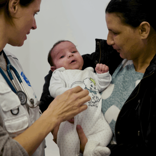 München: Ein Baby auf dem Arm einer Frau wird von einer Ärztin untersucht. Ärzte der Welt leistet medizinische Hilfe in Deutschland. © Til Mayer