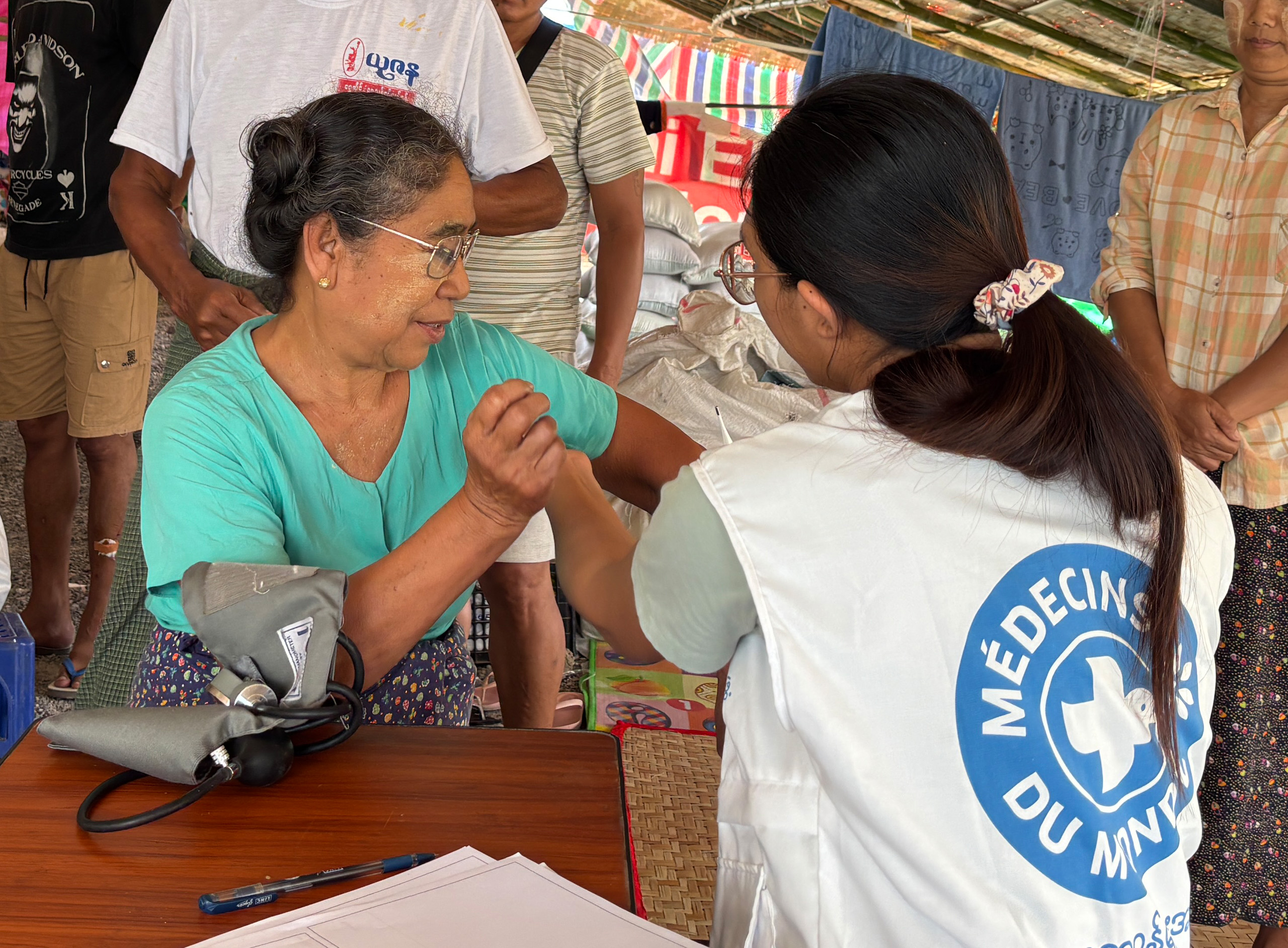 Eine mobile Klinik in Myanmar: Eine Mitarbeiterin von Ärzte der Welt spricht mit einer Patientin. Um sie herum stehen weitere Einwohner*innen. © Ärzte der Welt