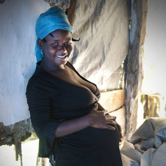 Eine schwangere Haitianerin hat ihre Hände über den Bauch gelegt und lächelt in die Kamera. © Pierre W. Henry
