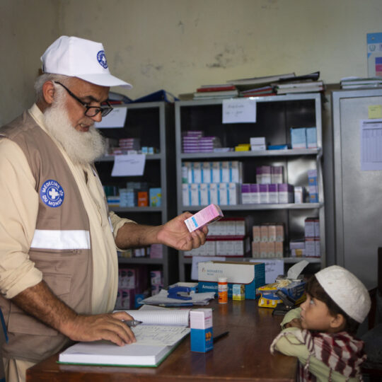 Pakistan: Ein Mitarbeiter von Ärzte der Welt hält eine Medikamentenpackung in der Hand, ein kleines Kind schaut ihn an. © Saiyna Bashir