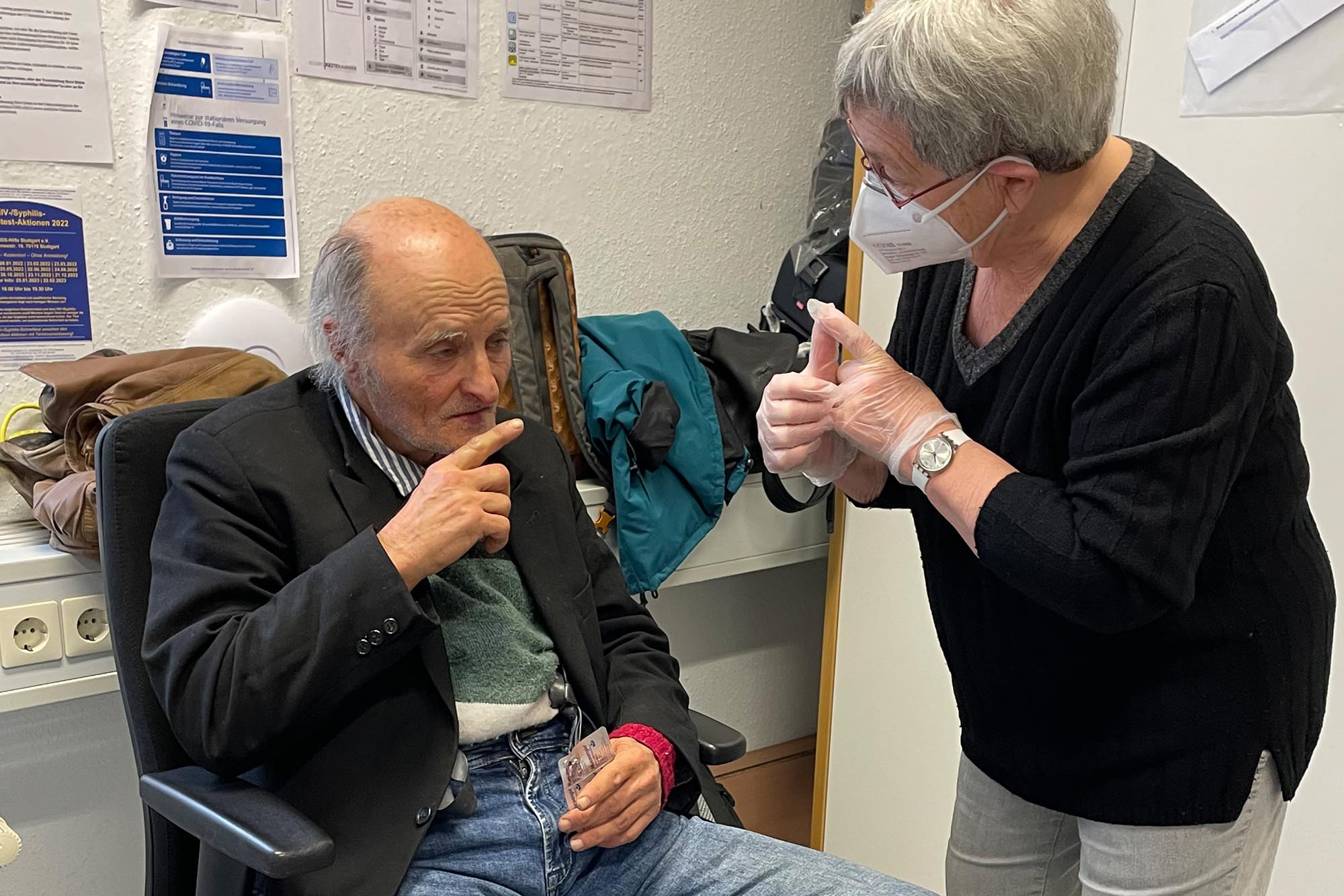 Eine Mitarbeiterin in Stuttgart, Deutschland, spricht mit einem Patienten, der auf einem Stuhl sitzt und eine Medikamentenpackung in der Hand hält. © Ärzte der Welt