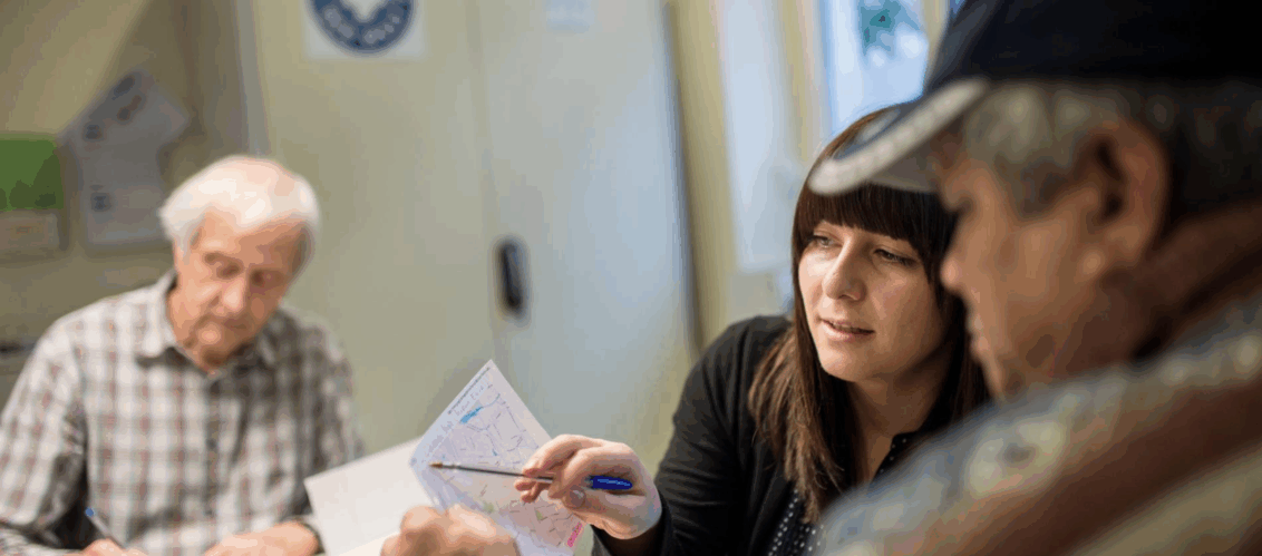 ©Bente_Stachowske Frau berät älteren Herren. Im hintergrund ist ein weiterer älterer Herr, welcher mit sich selbst beschäftigt zu sein.