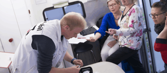 MedMobil in Stuttgart. Männlicher Arzt der im MedMobil etwas bearbeitet und 3 ältere Damen die ihm dabei zusehen