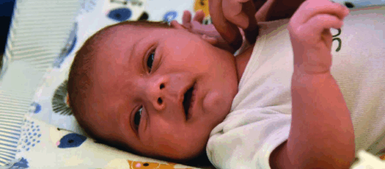 Ein Säugling liegt in der Krippe und schaut direkt in die Kamera