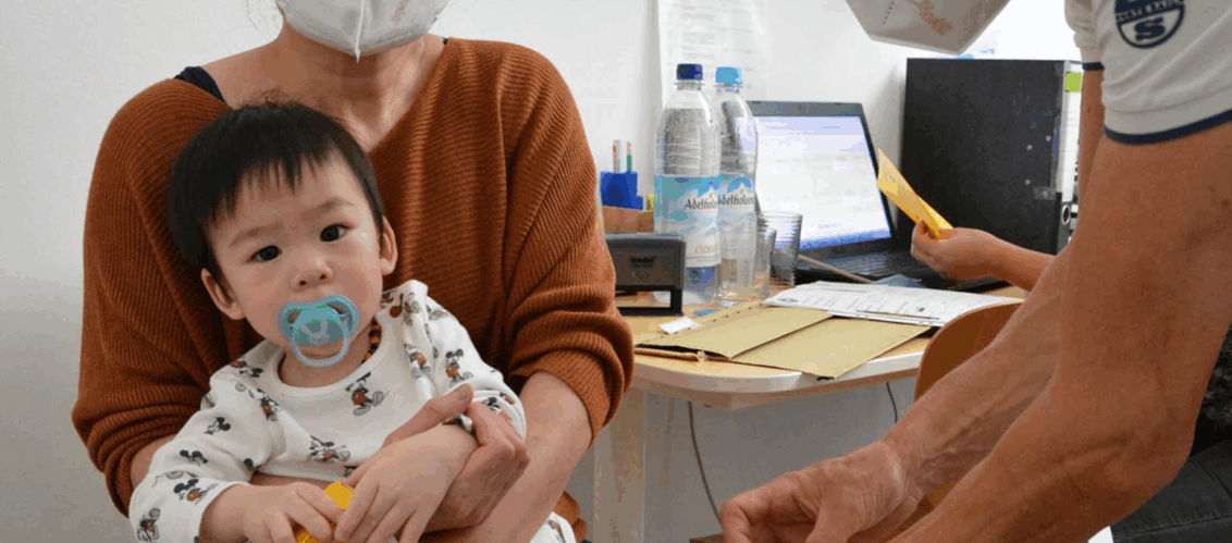 © aerzte der welt Ein sehr junges Kind und dessen Mutter befinden sich in einer medizinischen Sprechstunde mit open.med. Das Kind sitzt auf dem Schoß der Mutter und schaut in die Kamera