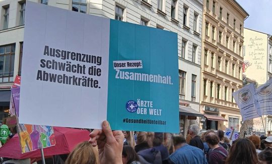 Eine Demonstrantin hält ein Plakat der Kampagne „Gesundheit ist unteilbar“ von Ärzte der Welt hoch. © Ärzte der Welt