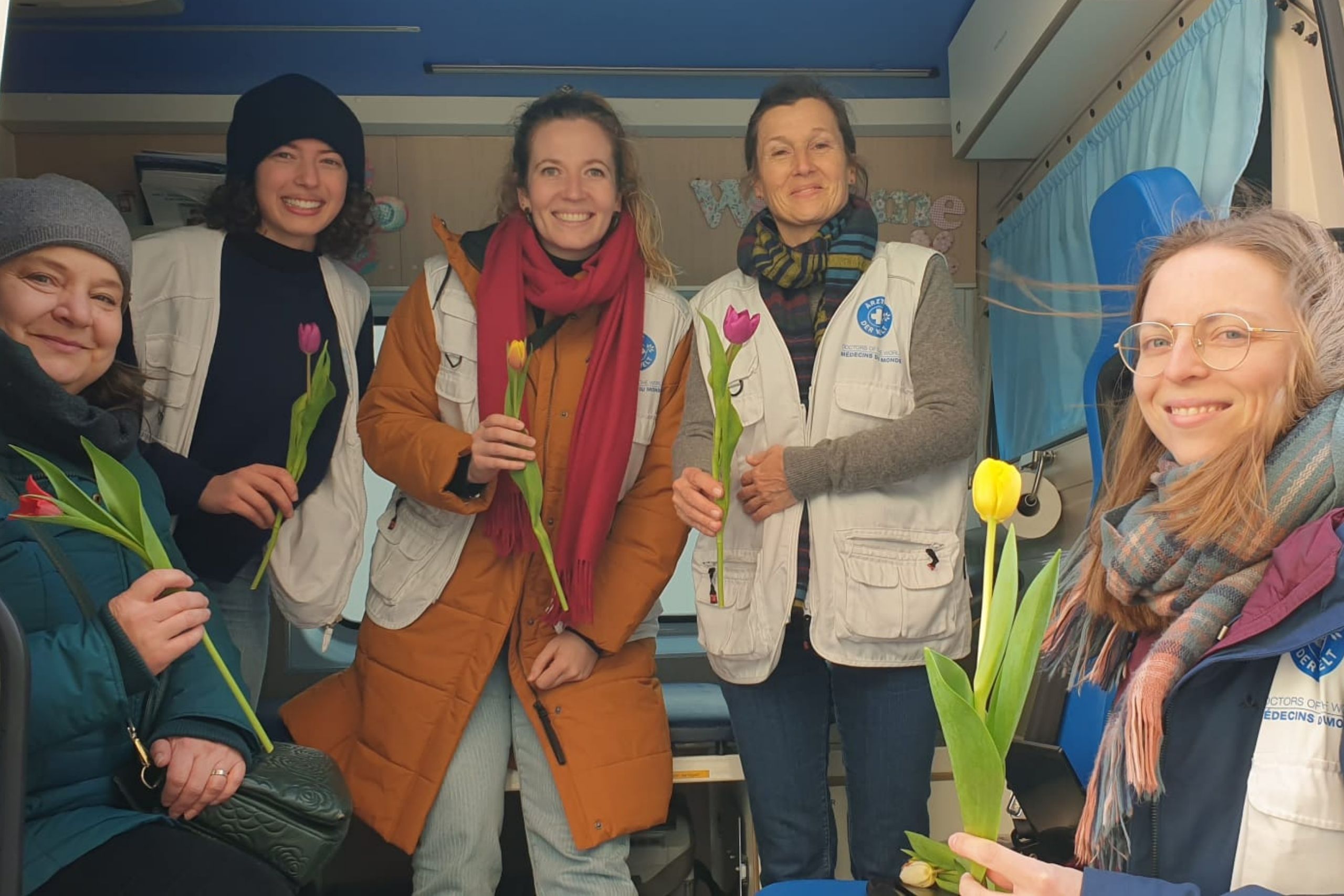 Mehrere Mitarbeiterinnen des Projekts open.med München halten lächelnd jeweils eine Blume in der Hand. © Ärzte der Welt