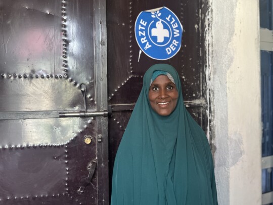 Eine Patientin posiert lächelnd vor der Kamera vor dem Eingang der Räumlichkeiten von Ärzte der Welt in der Region Somali in Äthiopien. © Ärzte der Welt