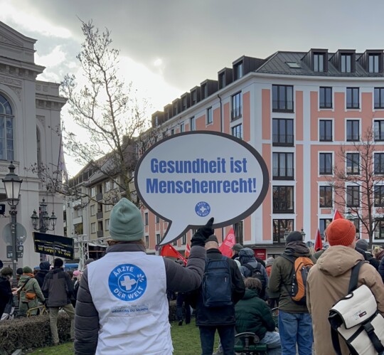 Eine Mitarbeiterin von „Ärzte der Welt“ hält bei einer Demonstration ein Schild mit der Aufschrift „Gesundheit ist ein Menschenrecht“ hoch. © Ärzte der Welt